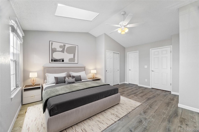 bedroom featuring ceiling fan, vaulted ceiling with skylight, wood finished floors, and baseboards