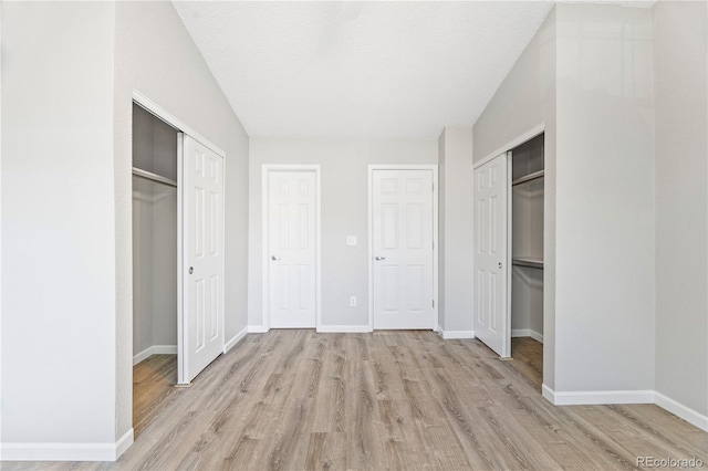 unfurnished bedroom featuring baseboards, a textured ceiling, light wood-style flooring, and multiple closets