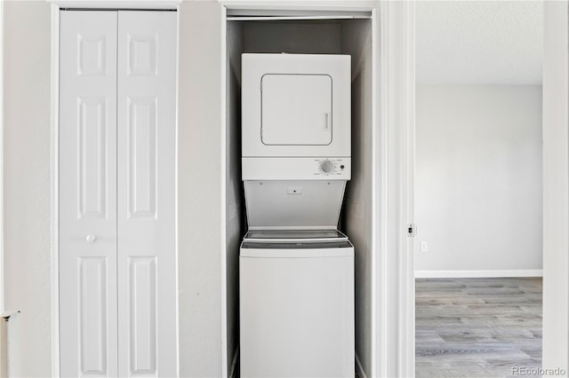 washroom featuring stacked washer / drying machine, a textured ceiling, wood finished floors, laundry area, and baseboards