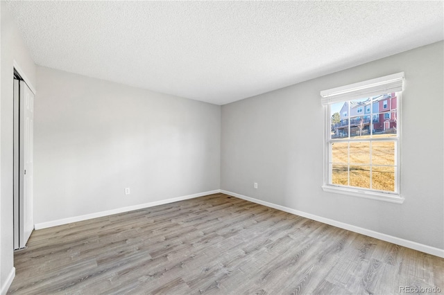 empty room featuring a textured ceiling, baseboards, and wood finished floors