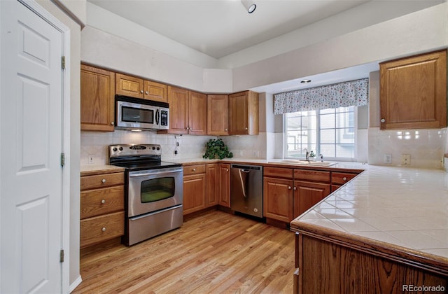 kitchen featuring kitchen peninsula, decorative backsplash, light hardwood / wood-style flooring, sink, and stainless steel appliances