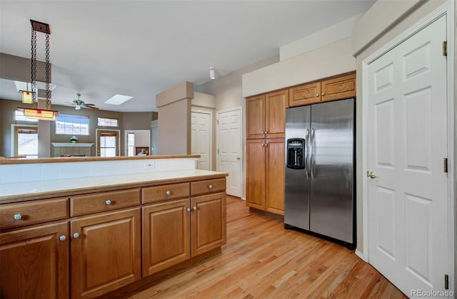 kitchen with light wood-type flooring, stainless steel fridge, ceiling fan, decorative light fixtures, and tile counters