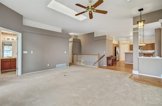 unfurnished living room with ceiling fan, a skylight, and light colored carpet