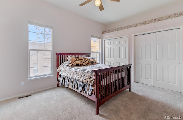 carpeted bedroom with two closets, multiple windows, and ceiling fan