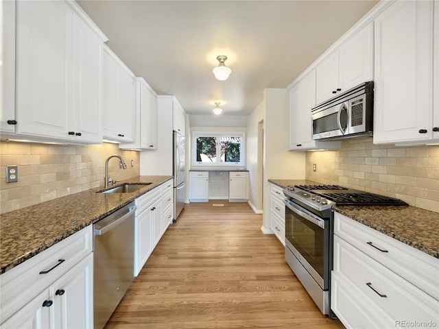 kitchen featuring white cabinets, appliances with stainless steel finishes, dark stone counters, and sink