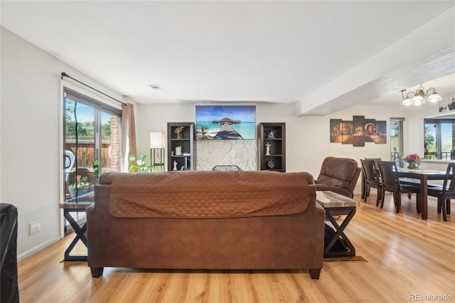 living room with plenty of natural light, light wood finished floors, a chandelier, and baseboards