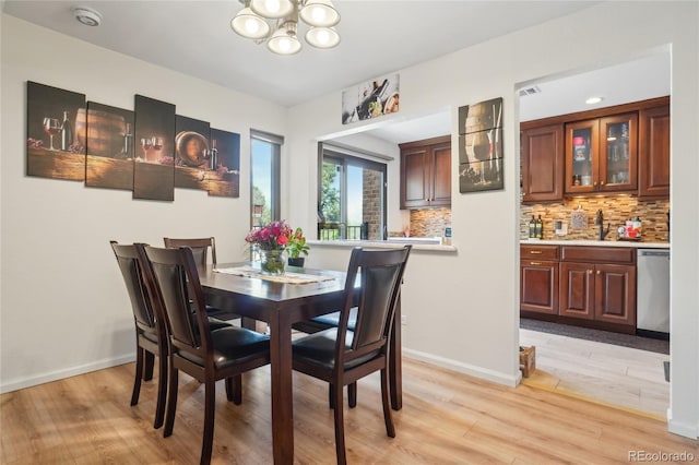 dining area with a chandelier, light wood-type flooring, wet bar, and baseboards