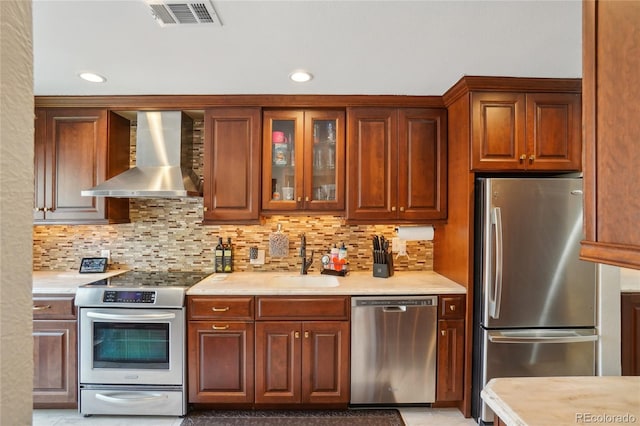 kitchen with stainless steel appliances, wall chimney exhaust hood, a sink, light countertops, and tasteful backsplash