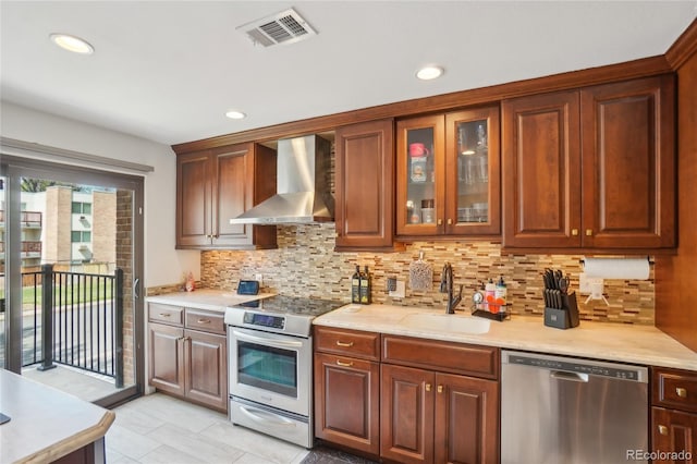 kitchen featuring stainless steel appliances, wall chimney range hood, a sink, light countertops, and light tile patterned floors