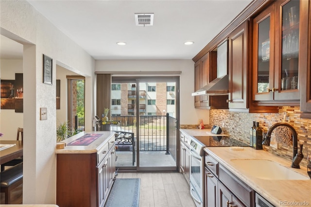 kitchen with wall chimney exhaust hood, electric stove, a sink, light countertops, and tasteful backsplash