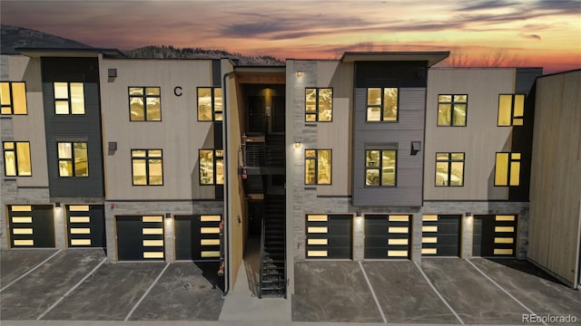 multi unit property featuring stone siding, stairway, and an attached garage