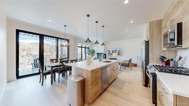 kitchen featuring pendant lighting, stainless steel appliances, light countertops, a kitchen island with sink, and a sink