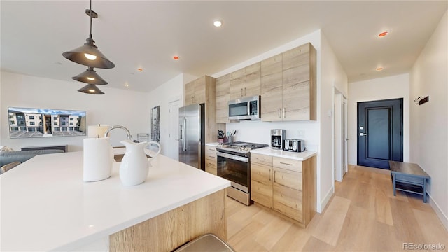 kitchen featuring stainless steel appliances, light countertops, hanging light fixtures, light brown cabinets, and modern cabinets