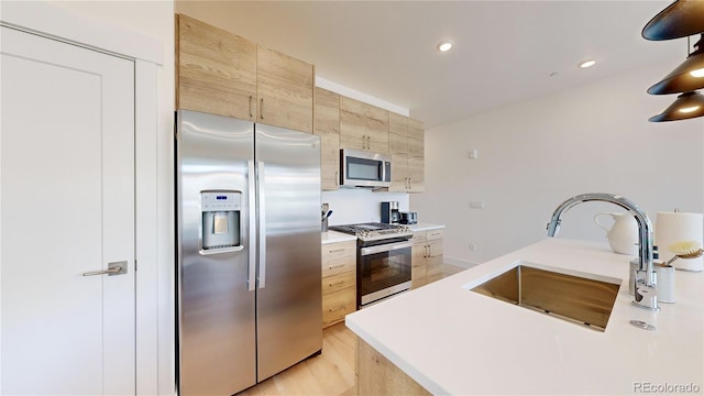 kitchen featuring modern cabinets, stainless steel appliances, light countertops, light brown cabinetry, and a sink