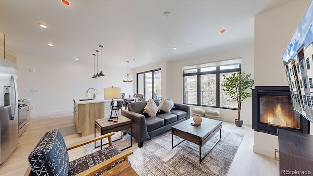 living area with recessed lighting, light wood finished floors, a multi sided fireplace, and an inviting chandelier