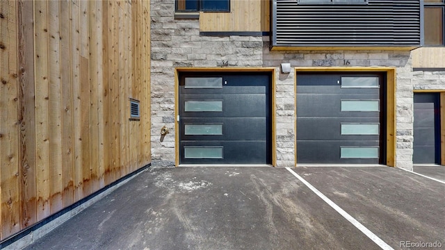 entrance to property with a garage, stone siding, and visible vents