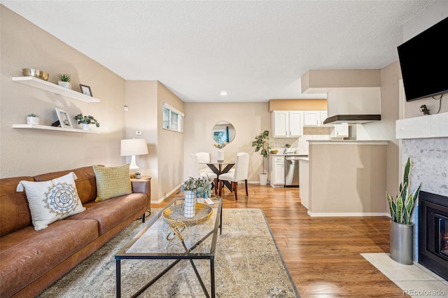 living room featuring a textured ceiling, a fireplace, light wood-style flooring, and baseboards