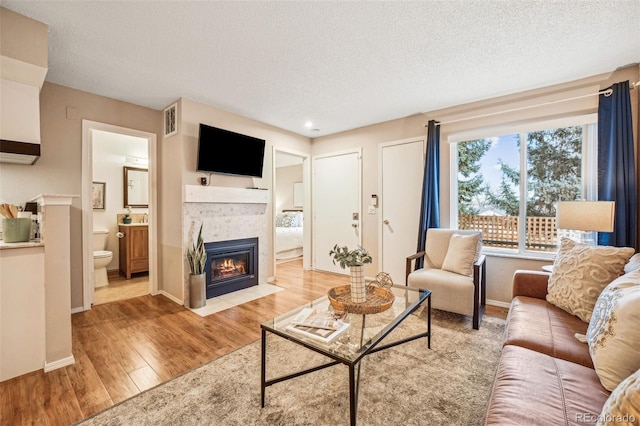 living area featuring light wood-type flooring, visible vents, a fireplace, and a textured ceiling