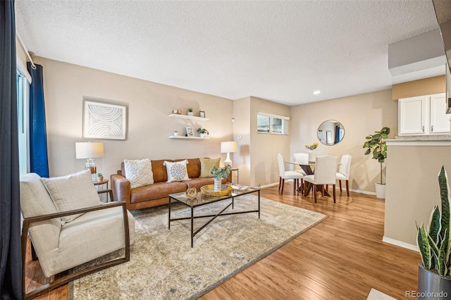 living area featuring light wood-type flooring, a textured ceiling, and baseboards