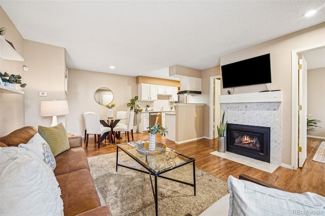 living area featuring light wood-style floors, a fireplace with flush hearth, baseboards, and recessed lighting