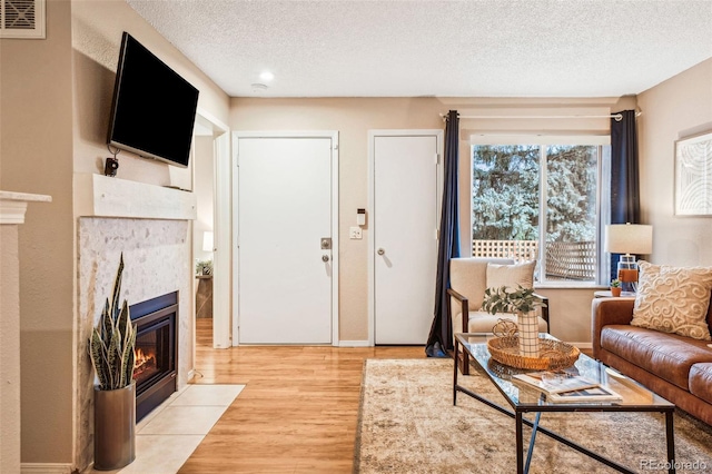 living area with a tile fireplace, visible vents, light wood-style flooring, and a textured ceiling