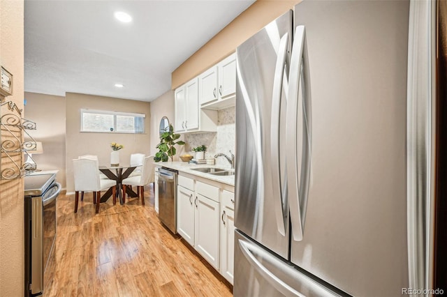 kitchen with appliances with stainless steel finishes, light wood-style floors, white cabinetry, and decorative backsplash