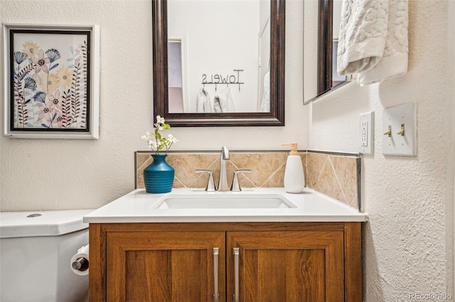 bathroom featuring a textured wall, vanity, and toilet