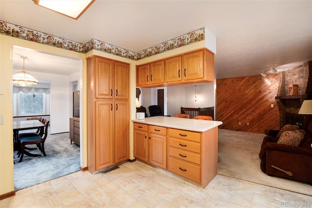 kitchen featuring kitchen peninsula, light carpet, hanging light fixtures, and wood walls