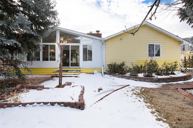 snow covered back of property with a sunroom