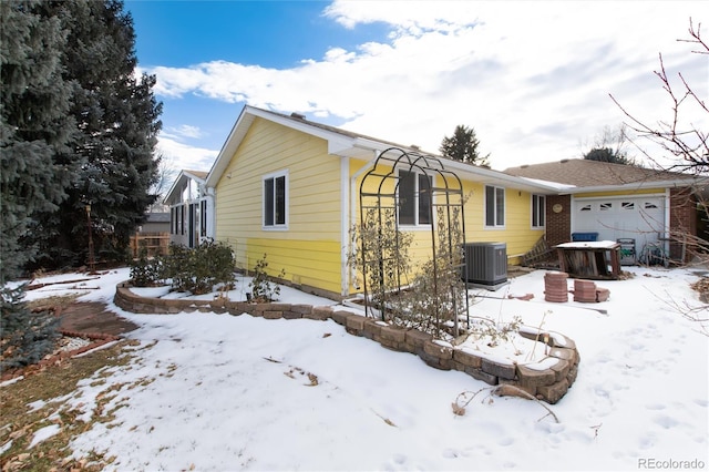 view of snowy exterior with a garage and central AC unit