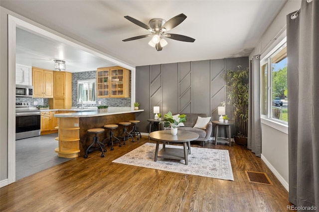 living area with wood finished floors, baseboards, visible vents, ceiling fan, and a decorative wall