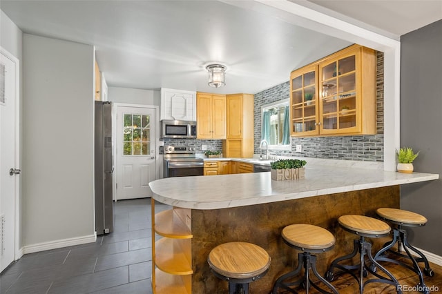 kitchen featuring a peninsula, a sink, light brown cabinetry, light countertops, and stainless steel appliances