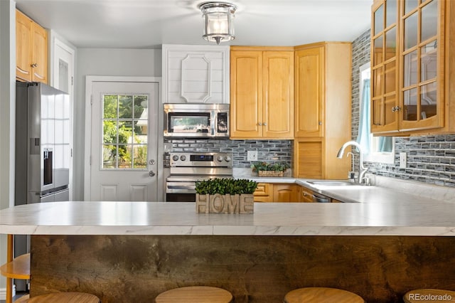 kitchen featuring decorative backsplash, appliances with stainless steel finishes, a breakfast bar, and a sink