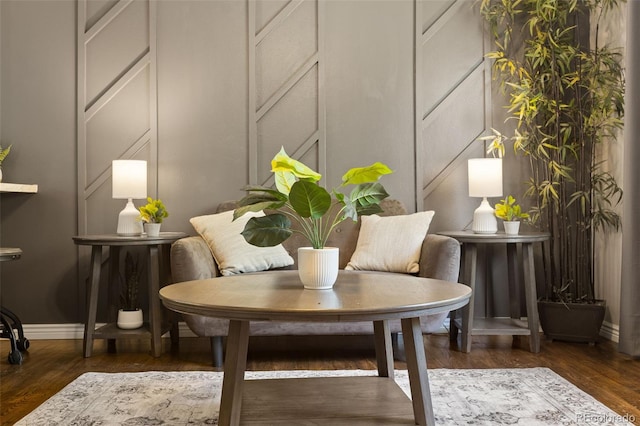 sitting room featuring baseboards, wood finished floors, and a decorative wall