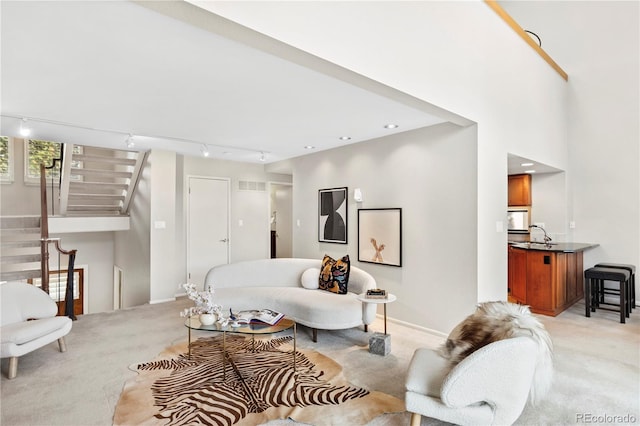 living room with a towering ceiling, light colored carpet, and track lighting