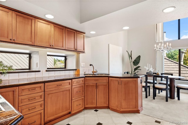 kitchen featuring kitchen peninsula, dark stone counters, sink, a chandelier, and light colored carpet