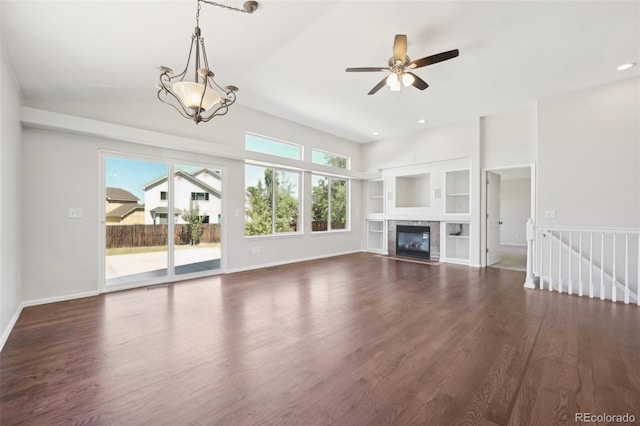 unfurnished living room featuring built in shelves, ceiling fan with notable chandelier, and dark hardwood / wood-style floors