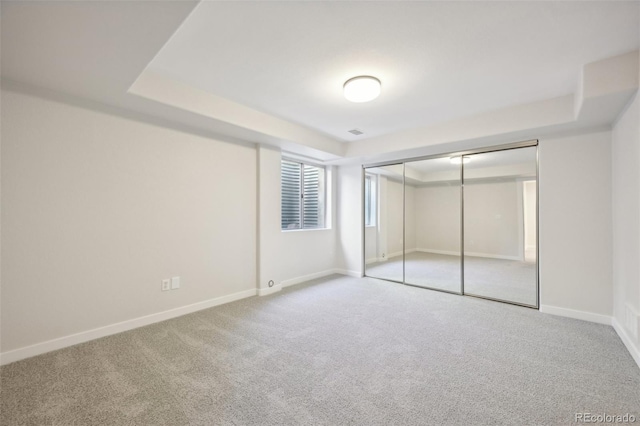 unfurnished bedroom with carpet, a raised ceiling, and a closet