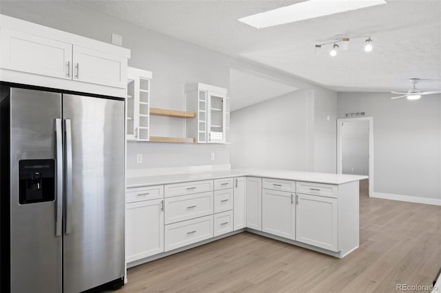 kitchen featuring stainless steel fridge with ice dispenser, vaulted ceiling with skylight, kitchen peninsula, and white cabinets
