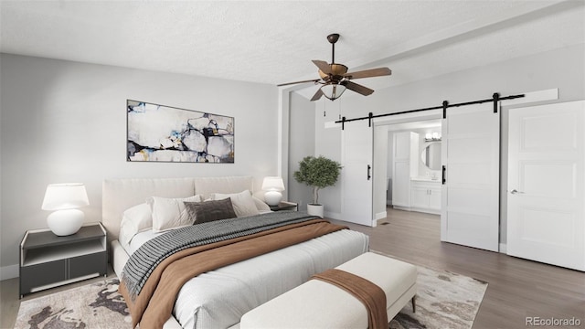 bedroom featuring ensuite bath, wood-type flooring, a textured ceiling, ceiling fan, and a barn door