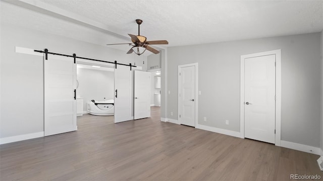 unfurnished bedroom with a barn door, hardwood / wood-style floors, and a textured ceiling