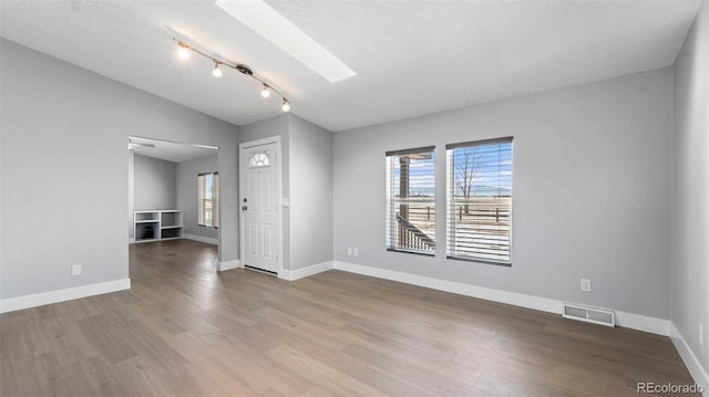 unfurnished room featuring hardwood / wood-style flooring, lofted ceiling with skylight, and a textured ceiling