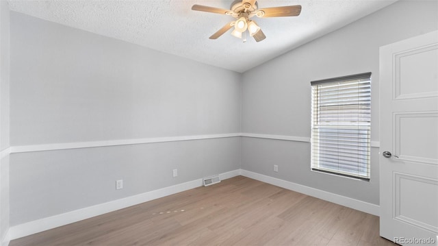 empty room with ceiling fan, lofted ceiling, a textured ceiling, and light hardwood / wood-style flooring
