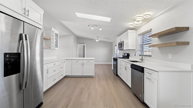 kitchen featuring sink, white cabinetry, stainless steel appliances, vaulted ceiling with skylight, and a textured ceiling