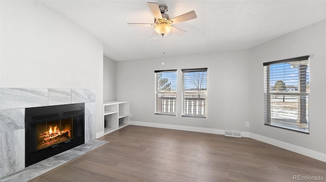 unfurnished living room with a tiled fireplace, hardwood / wood-style floors, a wealth of natural light, and ceiling fan