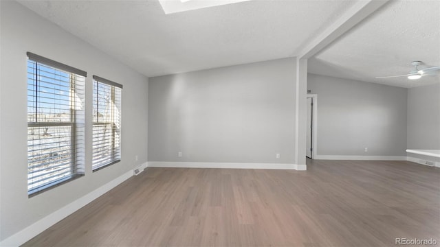 spare room featuring hardwood / wood-style floors, lofted ceiling with skylight, and a textured ceiling