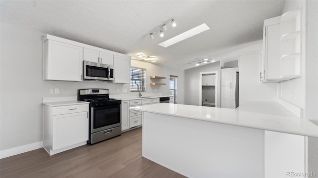 kitchen featuring sink, appliances with stainless steel finishes, vaulted ceiling with skylight, white cabinets, and kitchen peninsula