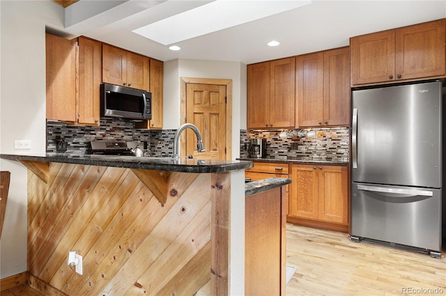 6773 Snowshoe Trl, Evergreen, CO 80439 - kitchen with appliances with stainless steel finishes, a skylight, a peninsula, light wood finished floors, and a breakfast bar