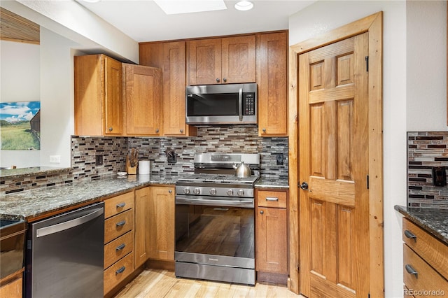 6773 Snowshoe Trl, Evergreen, CO 80439 - kitchen featuring appliances with stainless steel finishes, light wood-style floors, dark stone counters, and brown cabinets