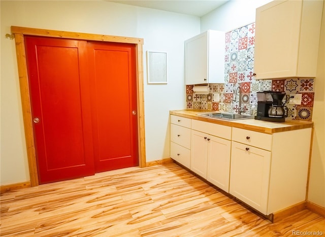kitchen with a sink, tasteful backsplash, light wood-style floors, white cabinets, and baseboards